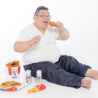 ジャンクフードを貪り食う膨よかな男性とビールの写真