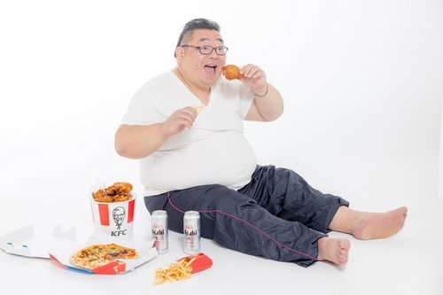 ジャンクフードを貪り食う膨よかな男性とビール