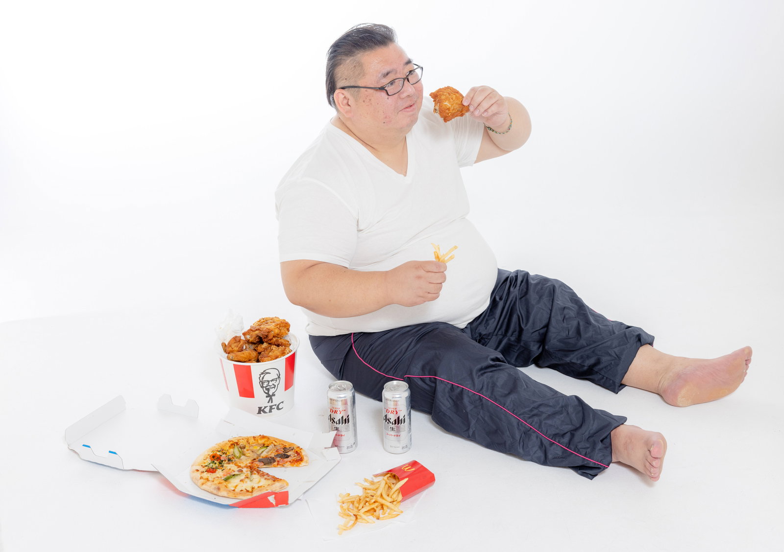 ファーストフードとビールを前に唐揚げを食べる肥満男性［モデル：ダルマ親方］