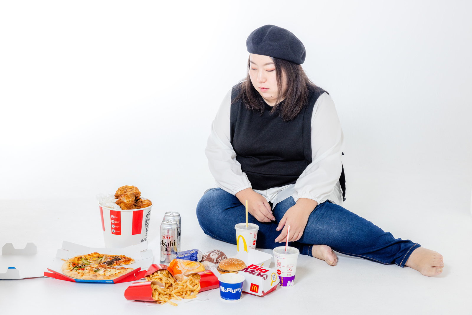 ファーストフードに囲まれ飲み物を持ちながら横座りする女性［モデル：KANA］