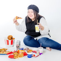 ジャンクフードに囲まれて暴飲暴食に目覚める女性の写真