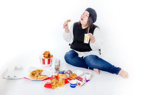 ファーストフードに囲まれた白い床でジャンクフードを食べる女性