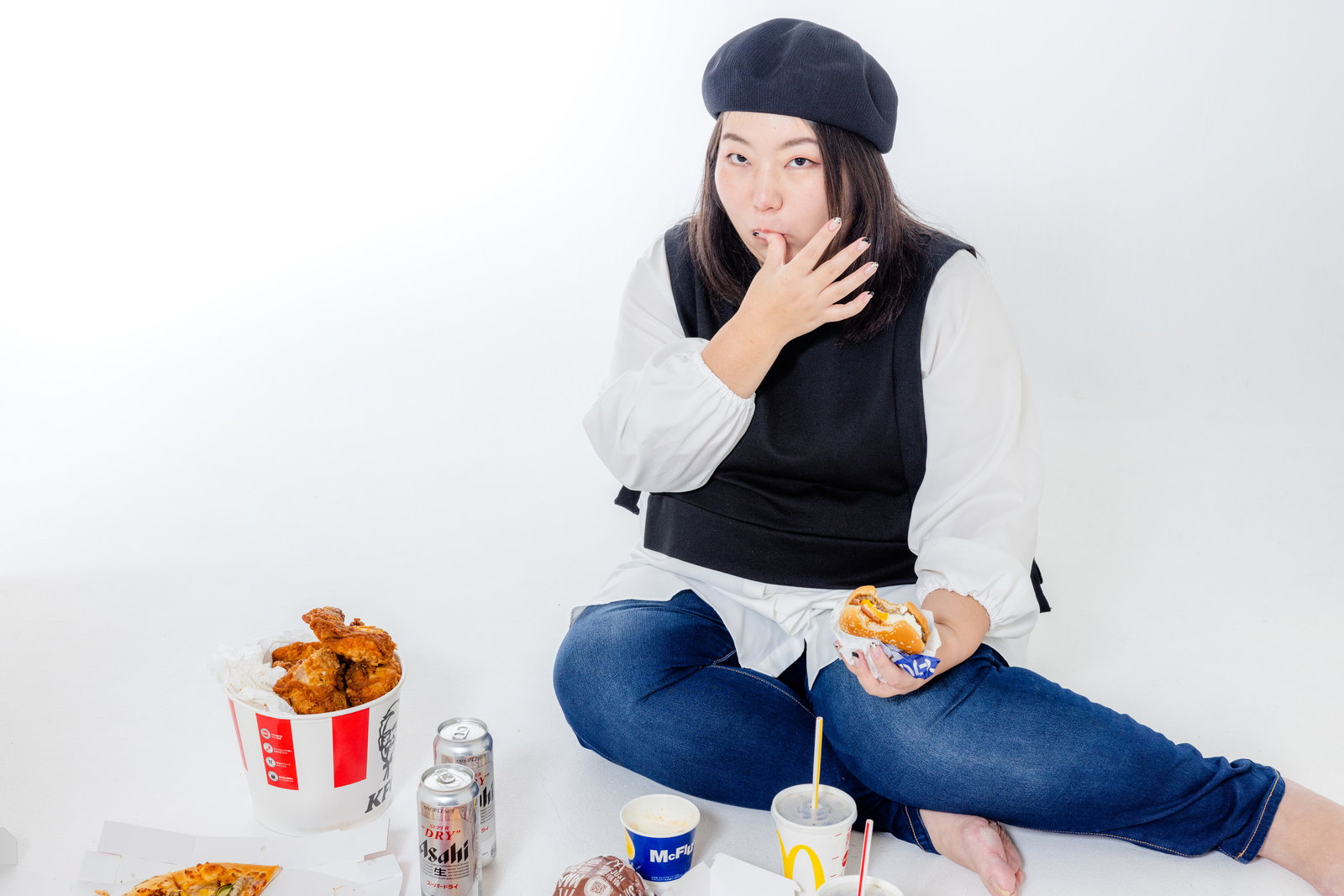 フライドチキンを手にしながら指を舐める女性がビールを飲んでいる［モデル：KANA］