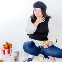 指を舐めながらジャンクフードを食べる女性の写真