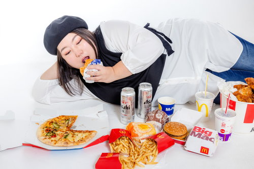 ジャンクフードに囲まれて食べる女性、ハンバーガーとポテトに囲まれた食卓