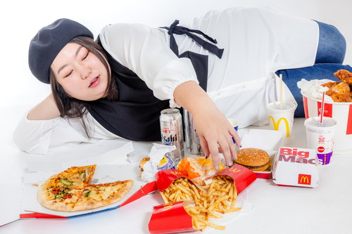 白いテーブルに広げたジャンクフードを前に横たわる女性