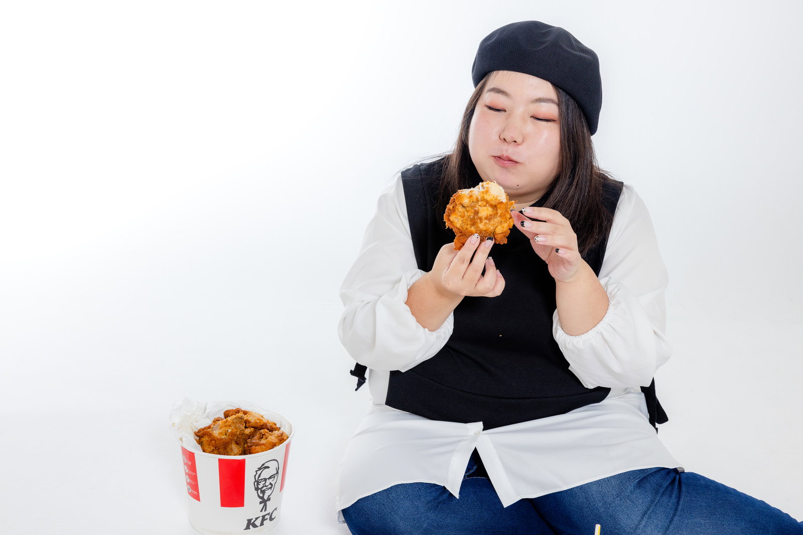 白背景でKFCのフライドチキンを食べる黒ベレー帽をかぶった女性［モデル：KANA］