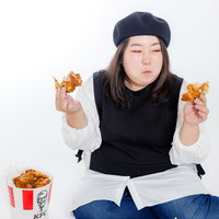 両手にフライドチキンを持つ女性、暴飲暴食とジャンクフードの写真