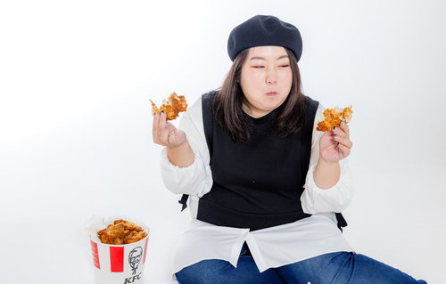 両手にフライドチキンを持つ女性、暴飲暴食とジャンクフード