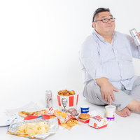 ジャンクフードに囲まれて胡坐をかいた膨よかな男性の写真