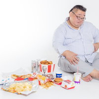 ジャンクフードに囲まれながら腰のぜい肉を掴む胡坐の男性の写真