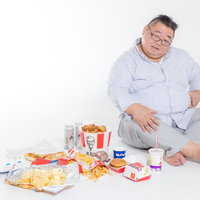 ジャンクフードを食べ過ぎてお腹を押さえる男性の写真
