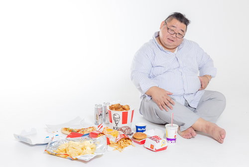 ジャンクフードを食べ過ぎてお腹を押さえる男性の写真