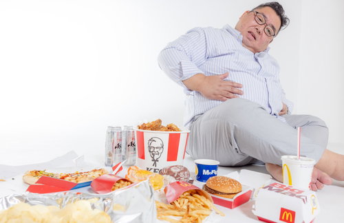 ジャンクフードを食べ過ぎてお腹を押さえる男性の写真
