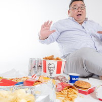 フードデリバリーで届いた大量のジャンクフードを前に驚く太った男性の写真