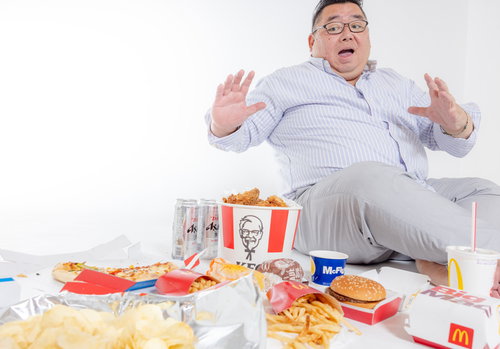 フードデリバリーで届いた大量のジャンクフードを前に驚く太った男性