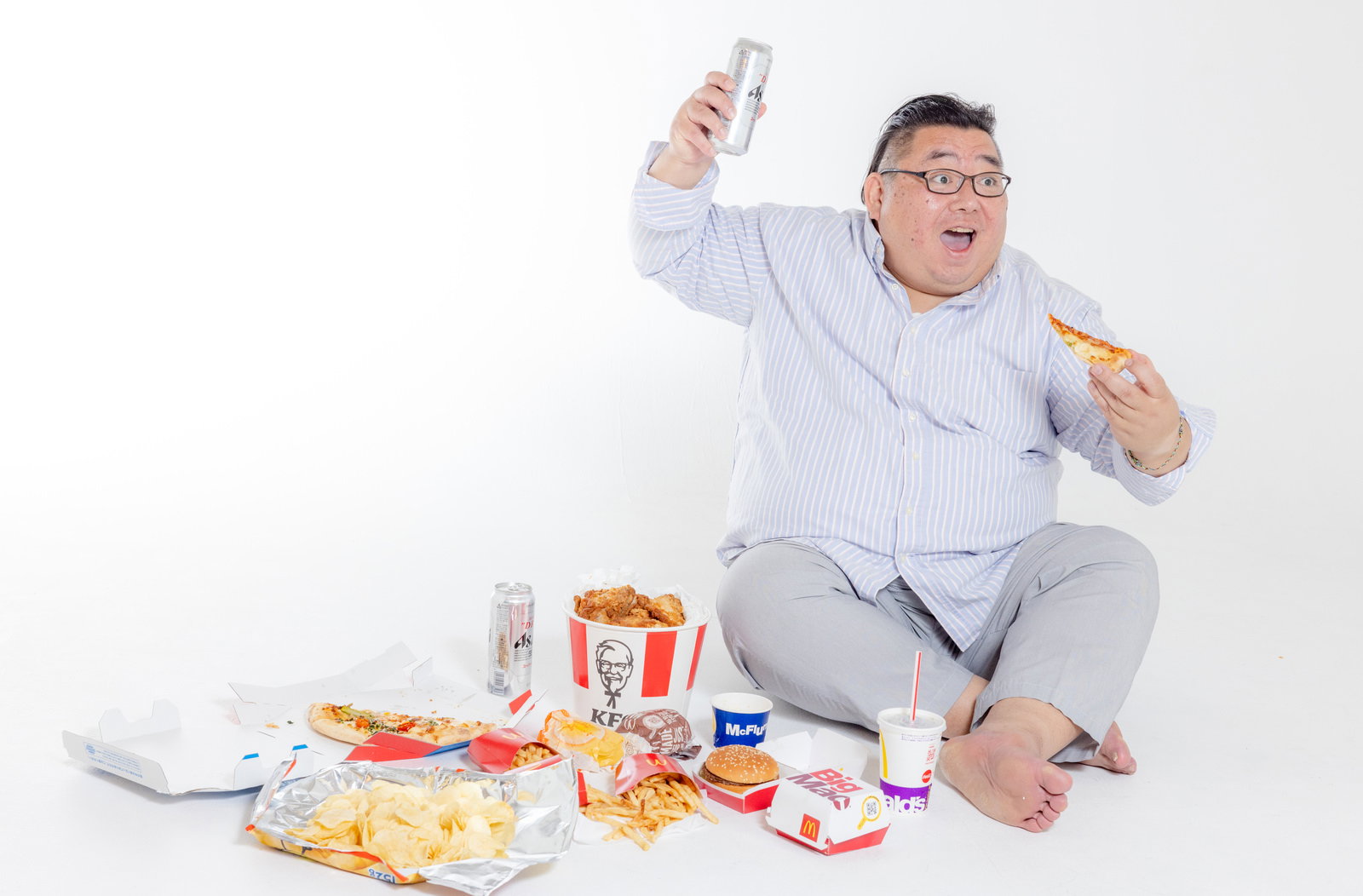 白いシャツの肥満男性がジャンクフードを食べながら飲料を飲んでいる［モデル：ダルマ親方］