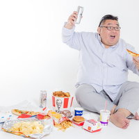ジャンクフードを食べながら観戦する肥満男性の写真