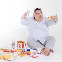 ジャンクフードを食べながら飲料を持つ膨よかな男性の写真