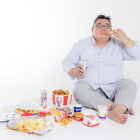 ジャンクフードを暴飲暴食する膨よかな男性の写真