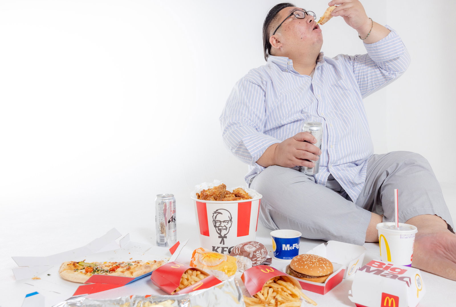 ファーストフードに囲まれ、揚げ物を食べる膨よかな男性［モデル：ダルマ親方］