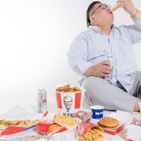 ダラダラと暴飲暴食するファーストフードに囲まれた膨よかな男性の写真
