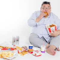 地べたに座り込んでファーストフードを暴食するメガネの男性の写真