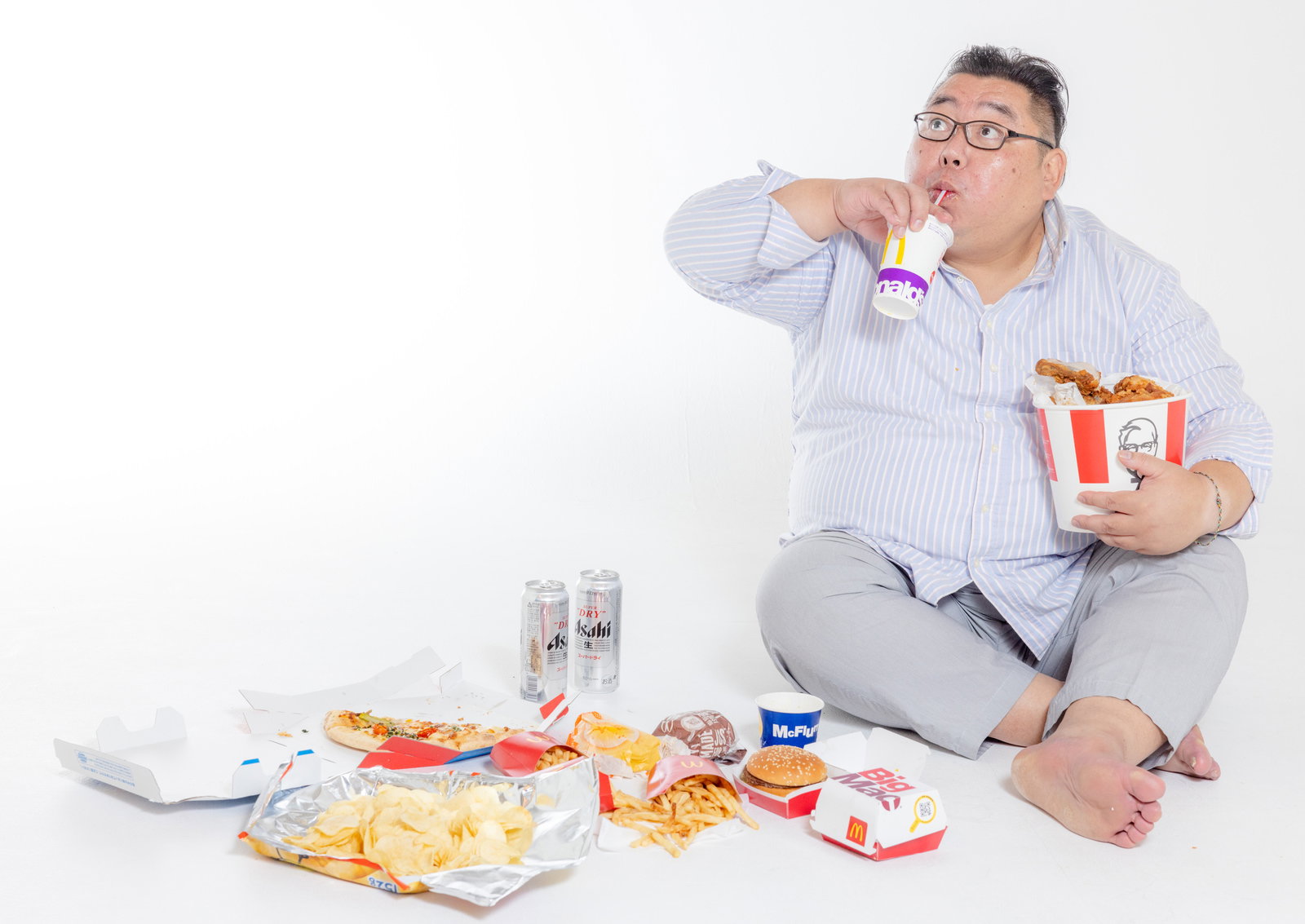床に座ってジャンクフードとドリンクに囲まれて飲食する男性［モデル：ダルマ親方］