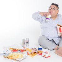 床座りで大量のジャンクフードを暴飲暴食する男性の写真