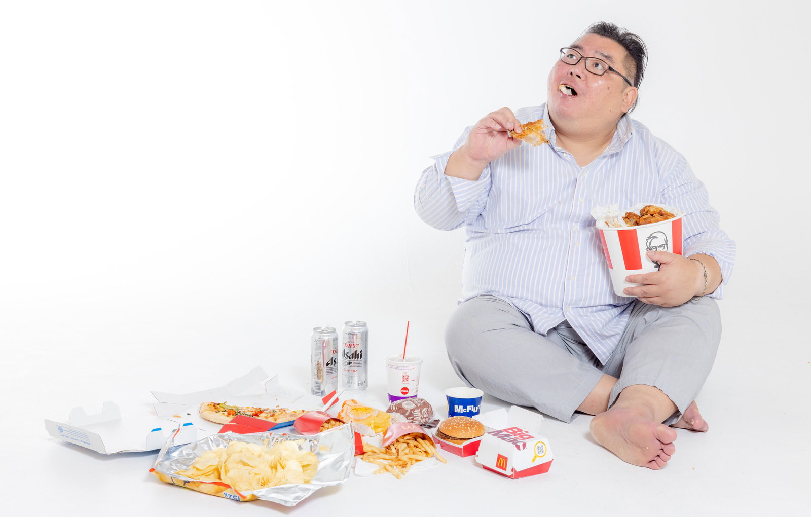 白いストライプシャツの男性がメガネをかけ、ケンタッキーフライドチキンを食べながらビール缶を持っている［モデル：ダルマ親方］