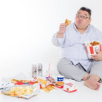 ケンタッキーフライドチキンを手に取るジャンクフードに囲まれた男性の写真