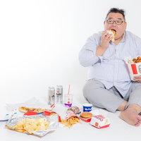 ハンバーガーを食べながらジャンクフードに囲まれた男性の写真