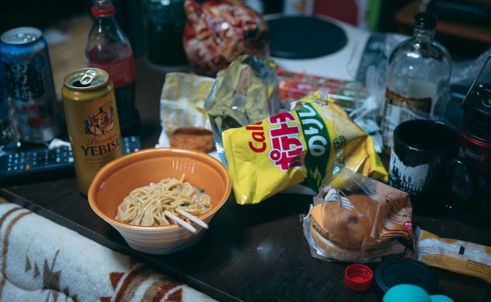 ゴミが散乱した部屋のテーブルの上にカップラーメンとビール瓶などが置かれている