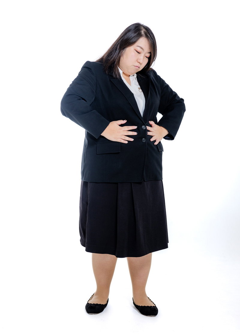 黒いスーツを着た膨よかな女性が両手でお腹を押さえている［モデル：KANA］