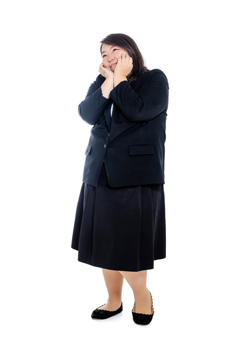 紺色のスーツを着たぽっちゃりした女性が両手で顔を包んで考え込んでいる［モデル：KANA］
