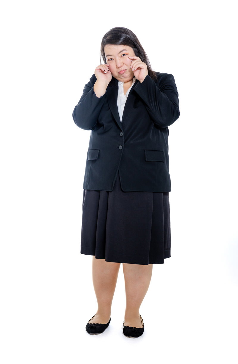 黒いスーツを着た女性が両手を頬に当てて泣きまねをしている［モデル：KANA］