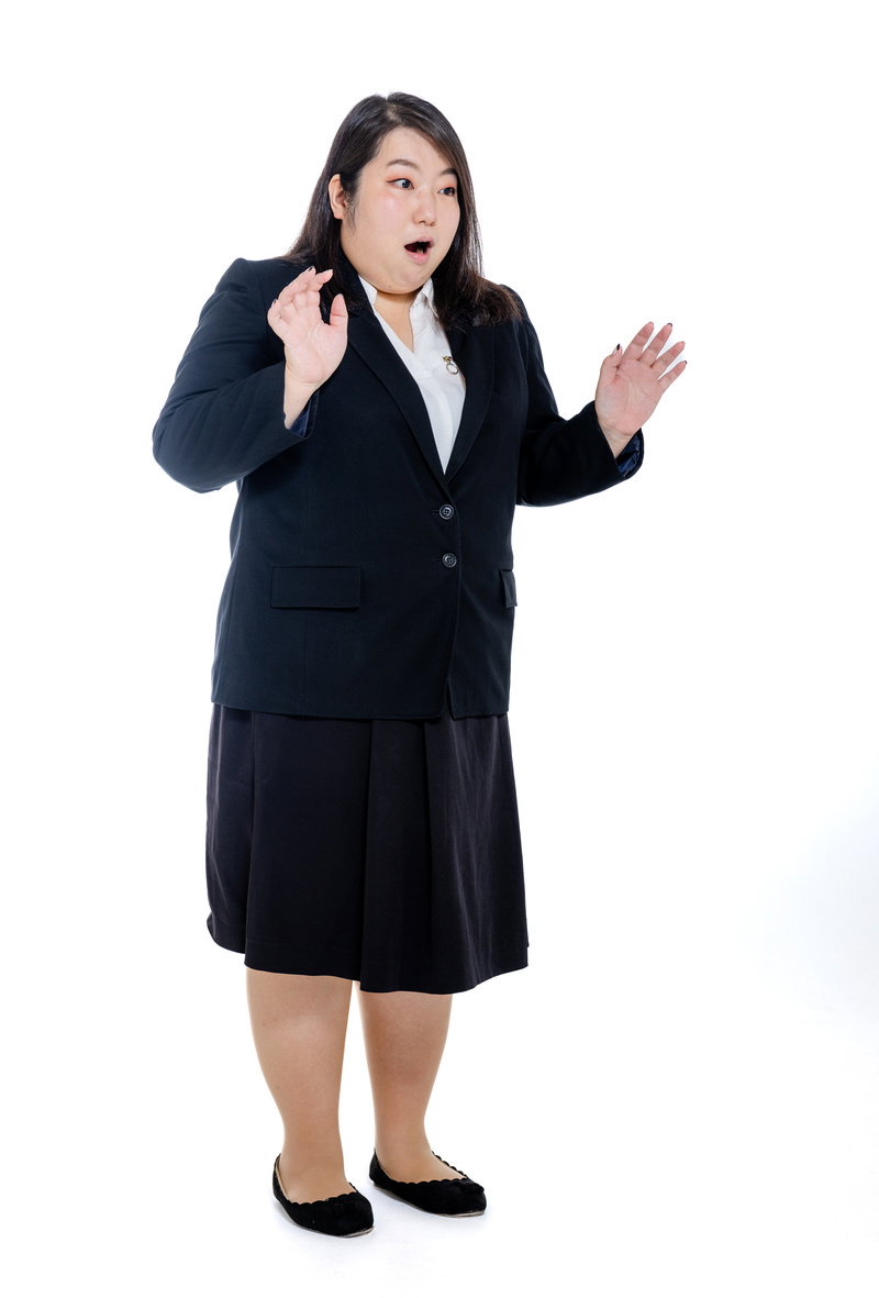 黒いスーツを着た女性が口を開けて驚いた表情で両手を広げている［モデル：KANA］