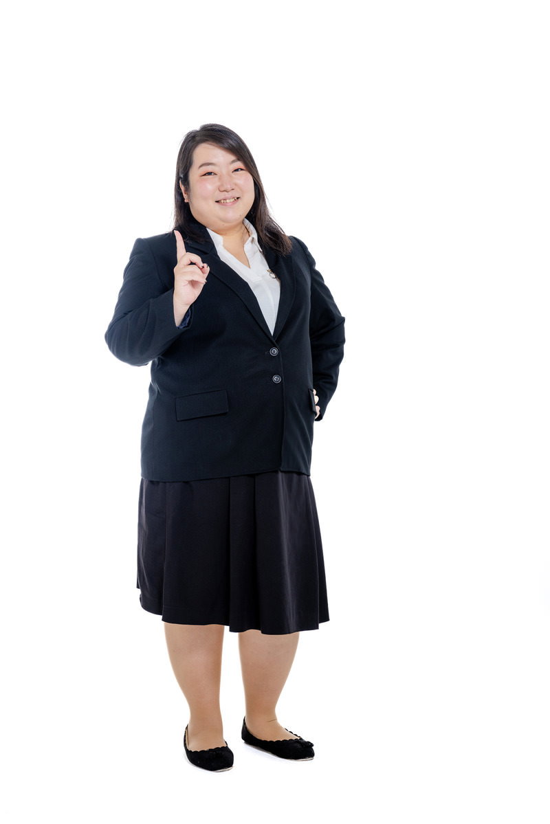 紺色のスーツを着た女性が人差し指を立てて1キロ痩せたことをアピール［モデル：KANA］