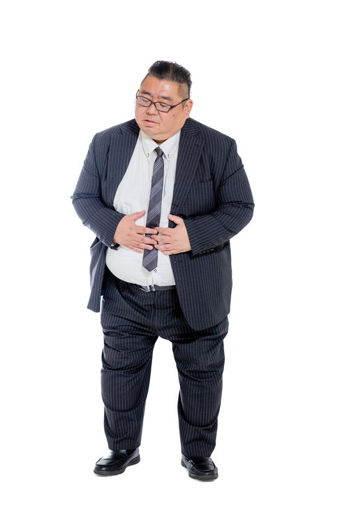 胃痛を訴えてお腹を押さえるスーツ着用の男性