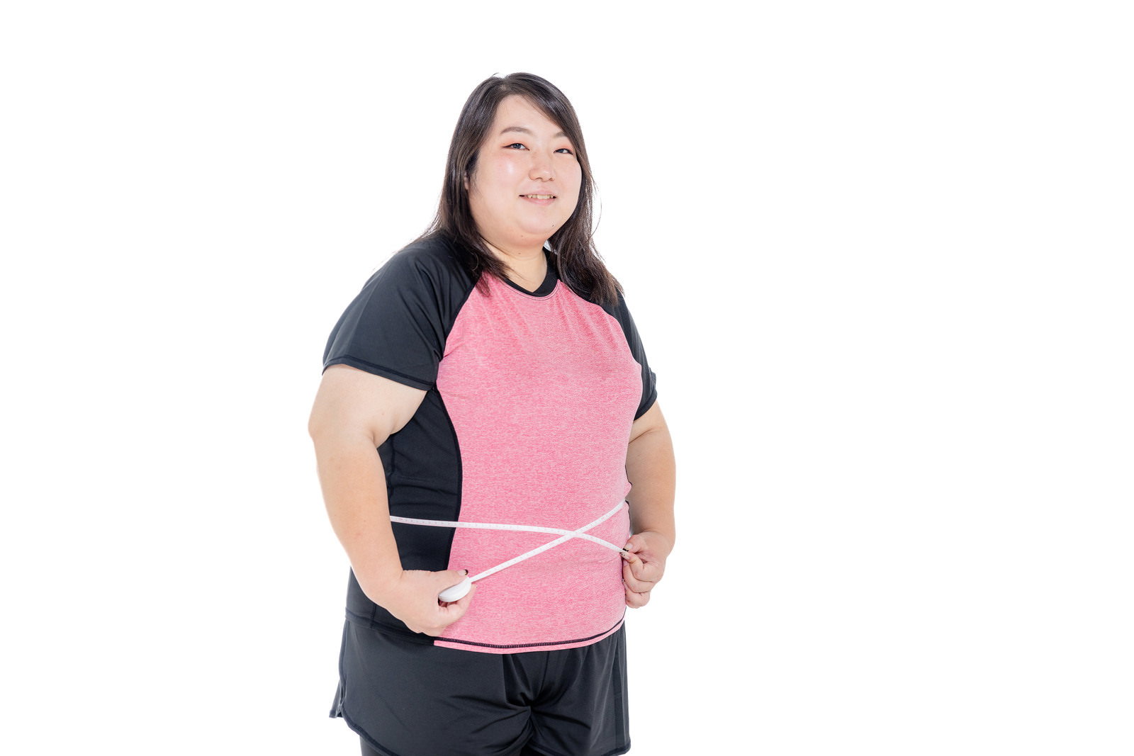 ピンクのTシャツを着た女性がウエストをメジャーで測定している［モデル：KANA］