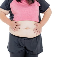 両手でお腹を摩る膨よかな女性のダイエットの写真