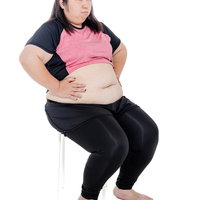 椅子に腰掛けてお腹に手を当てるダイエット中の女性の写真