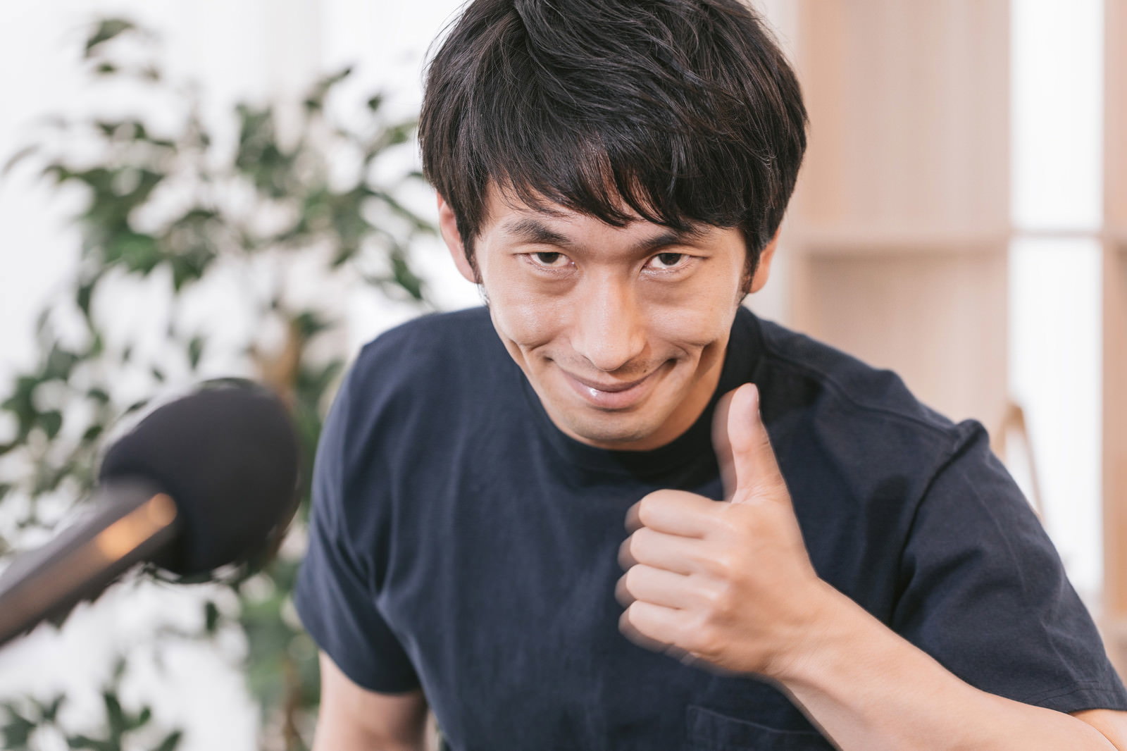 親指を立てて笑顔でサムズアップポーズを取る紺色Tシャツの男性［モデル：大川竜弥］