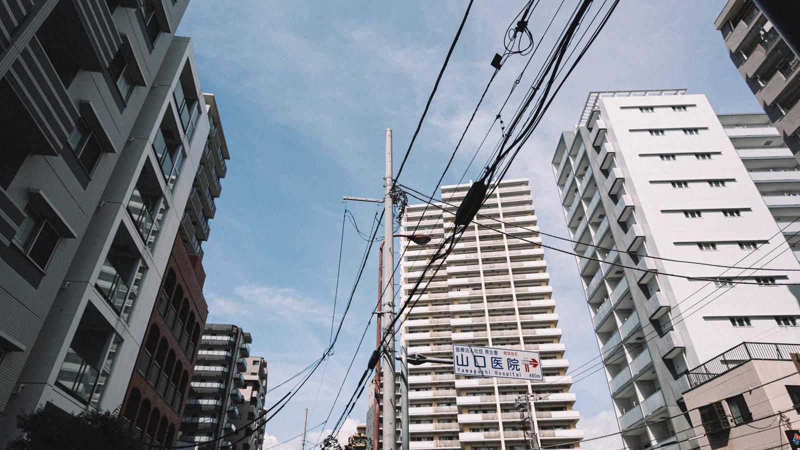 高層ビルと電線が交錯する都市の空を下から見上げた写真