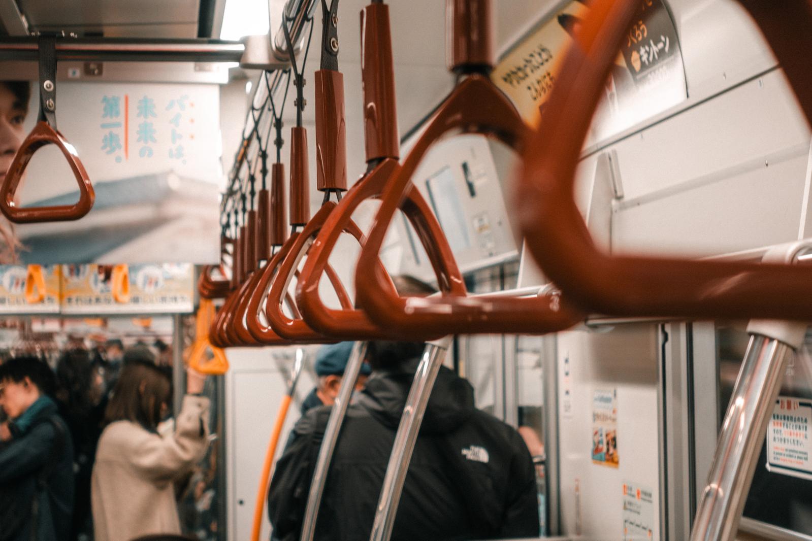 満員の電車車内で天井から下がる赤茶色の吊り革と乗客