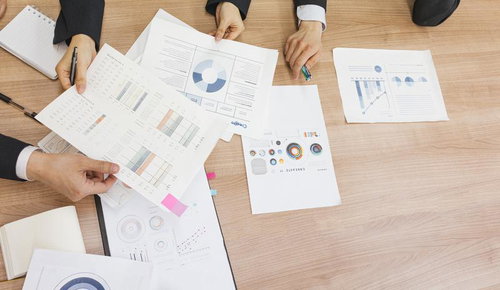 資料を手に取りオフィスで打ち合わせ会議をする複数人