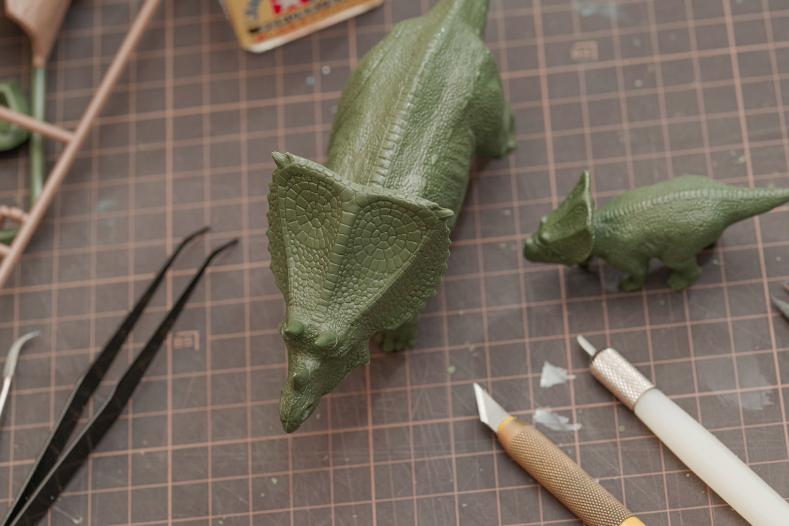 カッティングマット上に置かれた緑色の恐竜プラモデルと工具類