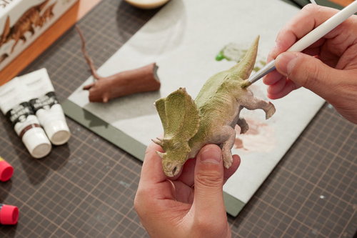 恐竜のプラモデルをドライブラシで陰影を強調する塗装作業