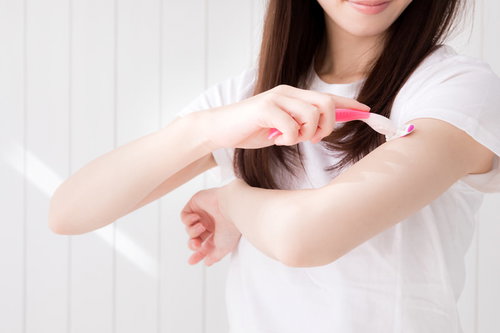 T字カミソリで肘上の腕を脱毛する色白の女性