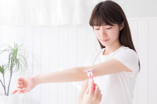 左腕を伸ばしてT字カミソリで脱毛する色白の女性